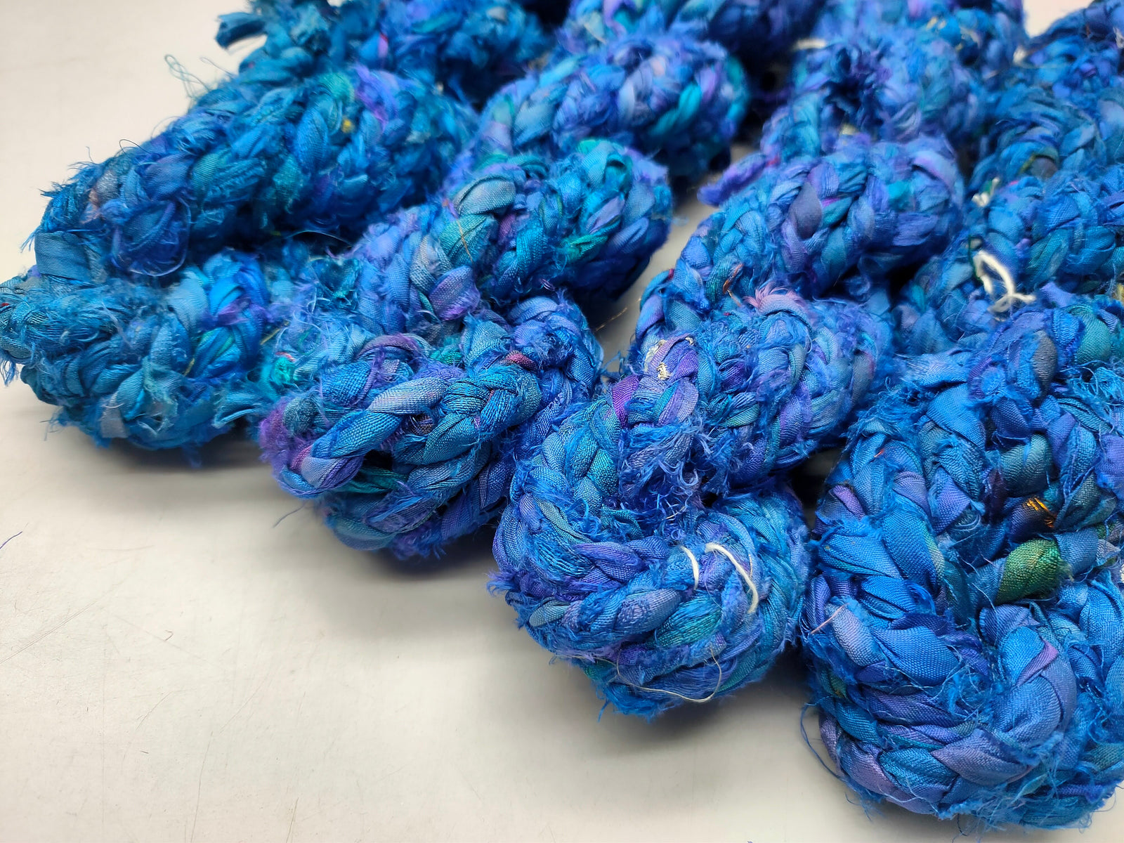 Braided Sari Silk Ribbon yarn is made of pure silk and is approximately an inch wide through out. Due to its handmade nature there might occasionally be variations in width. When silk fabric is cut and made into saris, wraps, and veils, there is always a bit left over. Rather than throw that waste fiber into the trash, it has been made into a beautiful, unique, soft yarn..!! Direct from India, this yarn is a truly recycled product. It is a bulky weight and is soft and easy to knit or croc