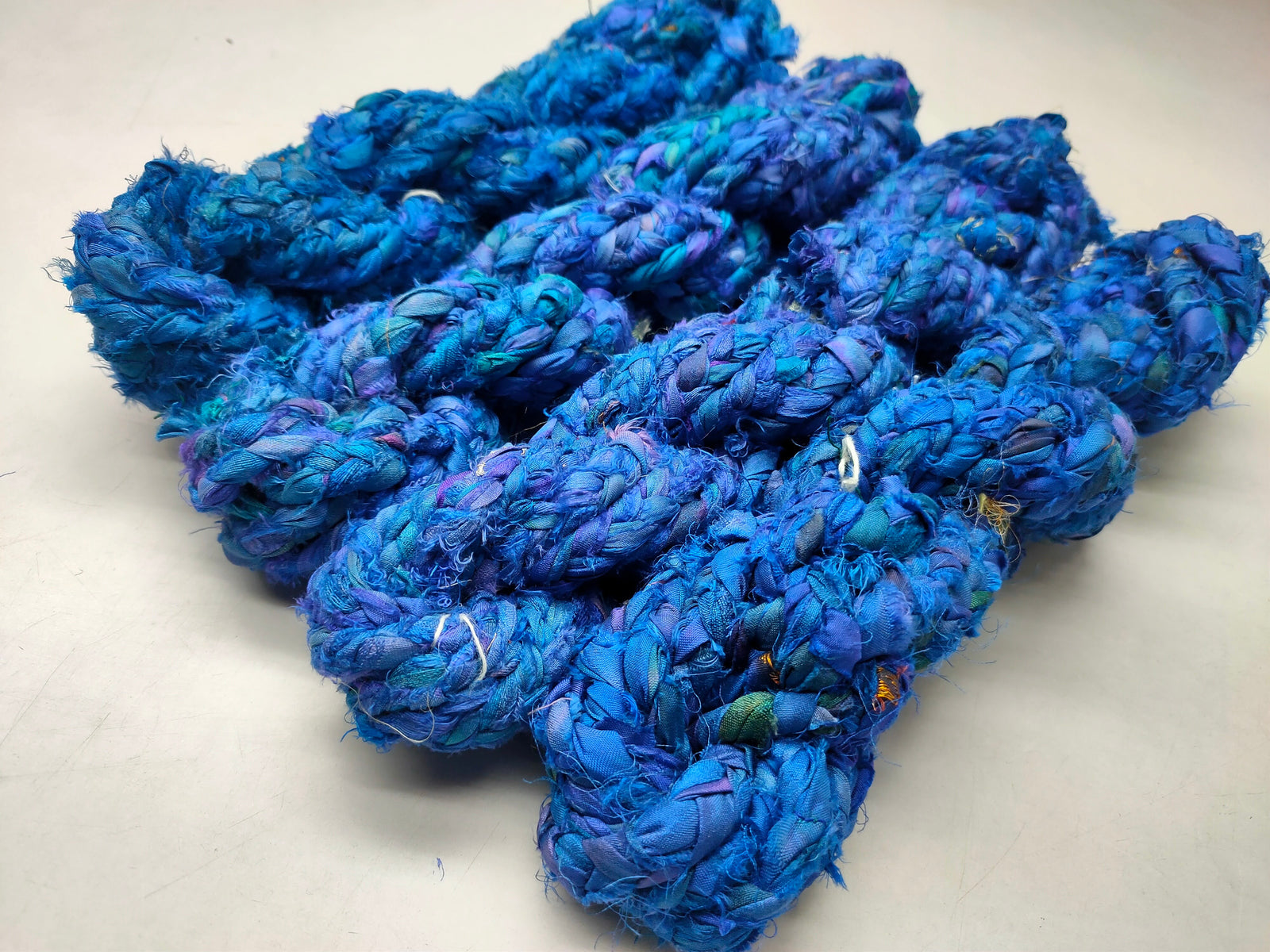 Braided Sari Silk Ribbon yarn is made of pure silk and is approximately an inch wide through out. Due to its handmade nature there might occasionally be variations in width. When silk fabric is cut and made into saris, wraps, and veils, there is always a bit left over. Rather than throw that waste fiber into the trash, it has been made into a beautiful, unique, soft yarn..!! Direct from India, this yarn is a truly recycled product. It is a bulky weight and is soft and easy to knit or croc