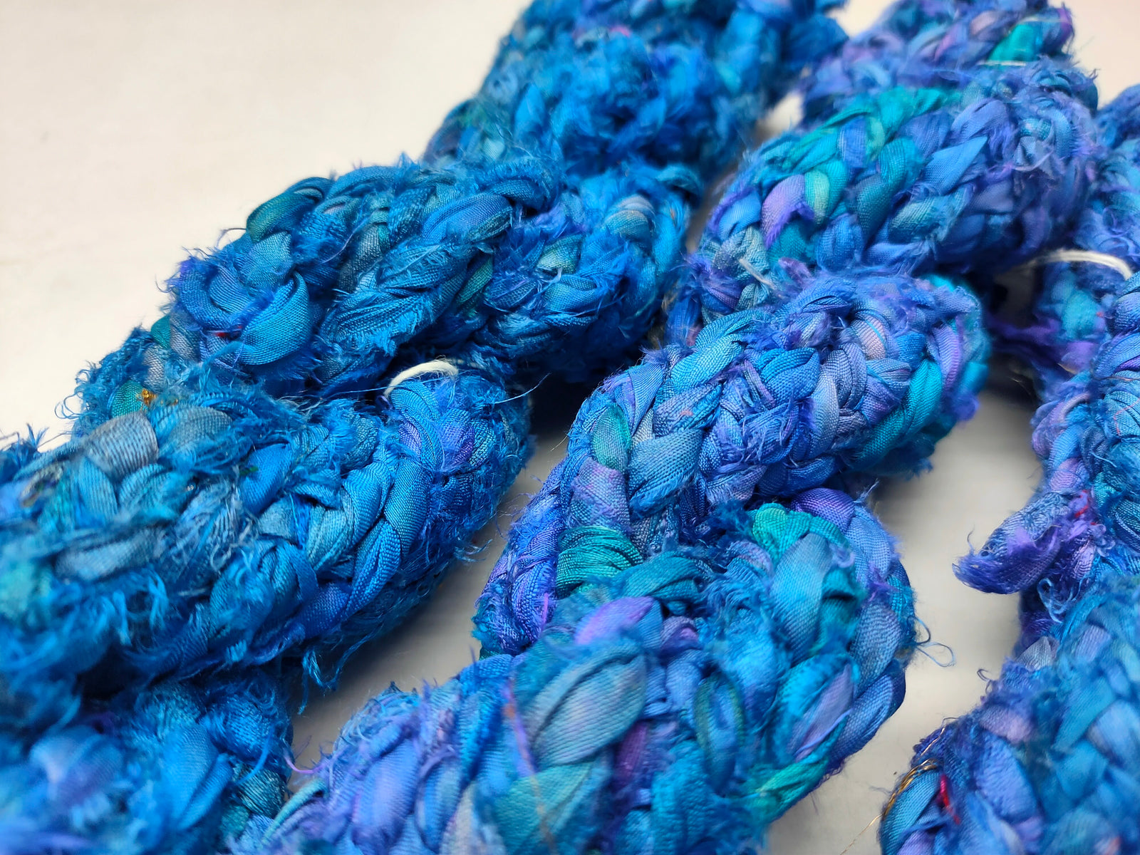 Braided Sari Silk Ribbon yarn is made of pure silk and is approximately an inch wide through out. Due to its handmade nature there might occasionally be variations in width. When silk fabric is cut and made into saris, wraps, and veils, there is always a bit left over. Rather than throw that waste fiber into the trash, it has been made into a beautiful, unique, soft yarn..!! Direct from India, this yarn is a truly recycled product. It is a bulky weight and is soft and easy to knit or croc