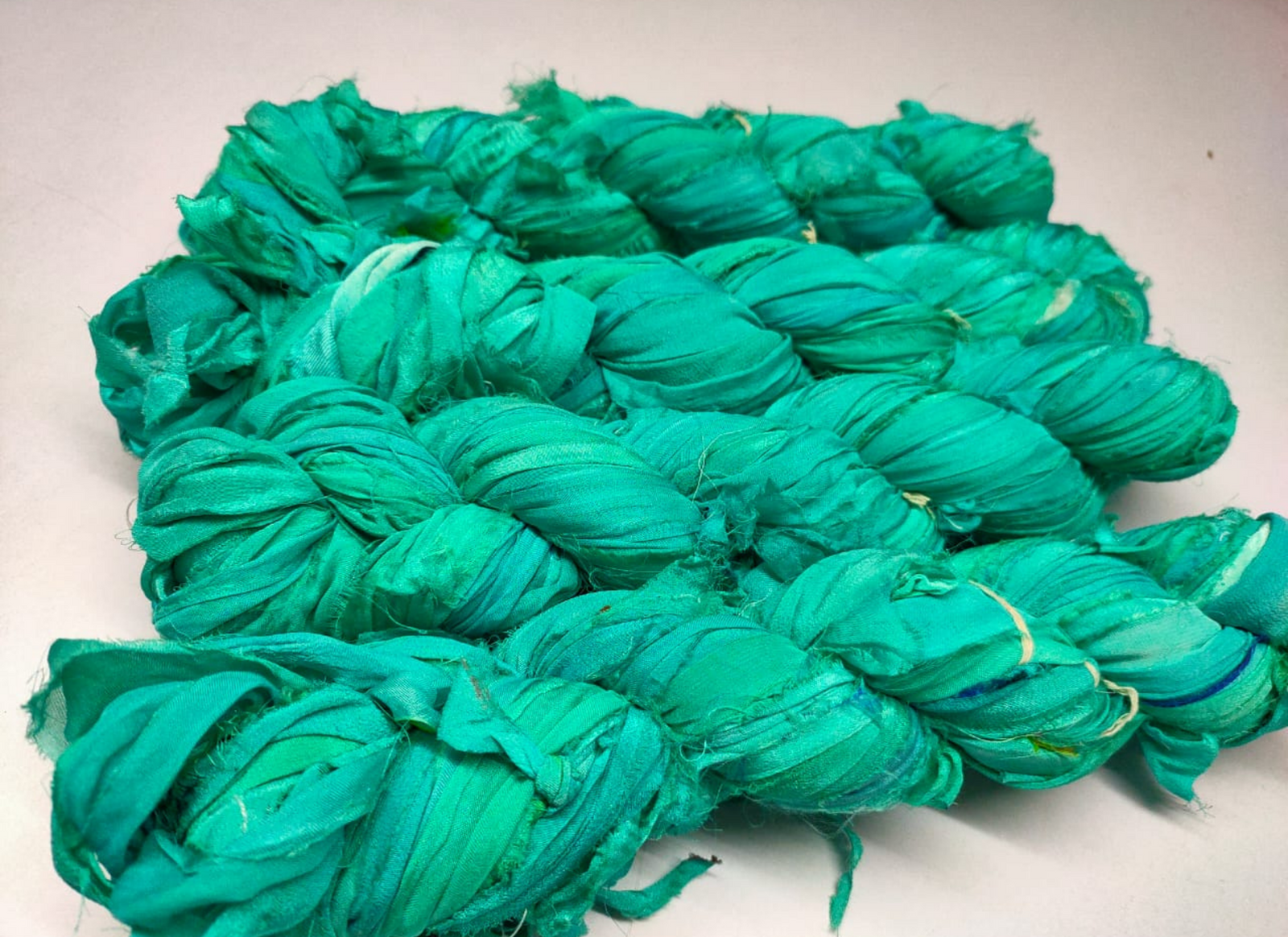 Chiffon Ribbon Yarn -  Turquoise Green is the by-product of saris that women wear in India. It is the loose ends of saris collected from industrial mills in India that is torn in stripes and sewn end to end to make beautiful and colorful ribbons. The vibrant colors and unique texture of these silk fabric, the Chiffon Ribbon are inspirational to designers, knitters, and artisans.