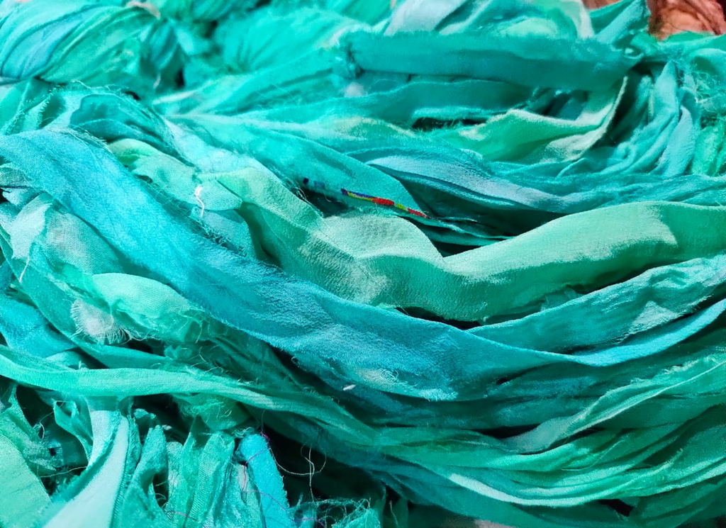 Chiffon Ribbon Yarn -  Turquoise Green is the by-product of saris that women wear in India. It is the loose ends of saris collected from industrial mills in India that is torn in stripes and sewn end to end to make beautiful and colorful ribbons. The vibrant colors and unique texture of these silk fabric, the Chiffon Ribbon are inspirational to designers, knitters, and artisans.
