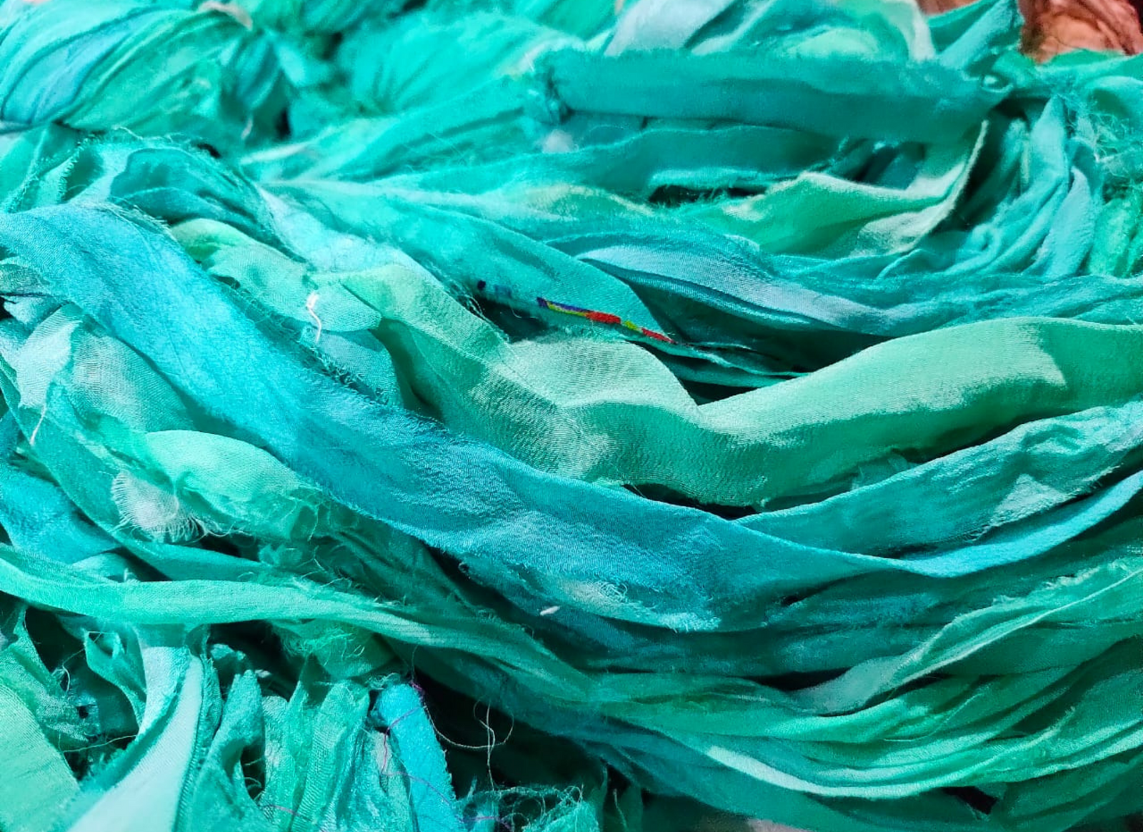 Chiffon Ribbon Yarn -  Turquoise Green is the by-product of saris that women wear in India. It is the loose ends of saris collected from industrial mills in India that is torn in stripes and sewn end to end to make beautiful and colorful ribbons. The vibrant colors and unique texture of these silk fabric, the Chiffon Ribbon are inspirational to designers, knitters, and artisans.
