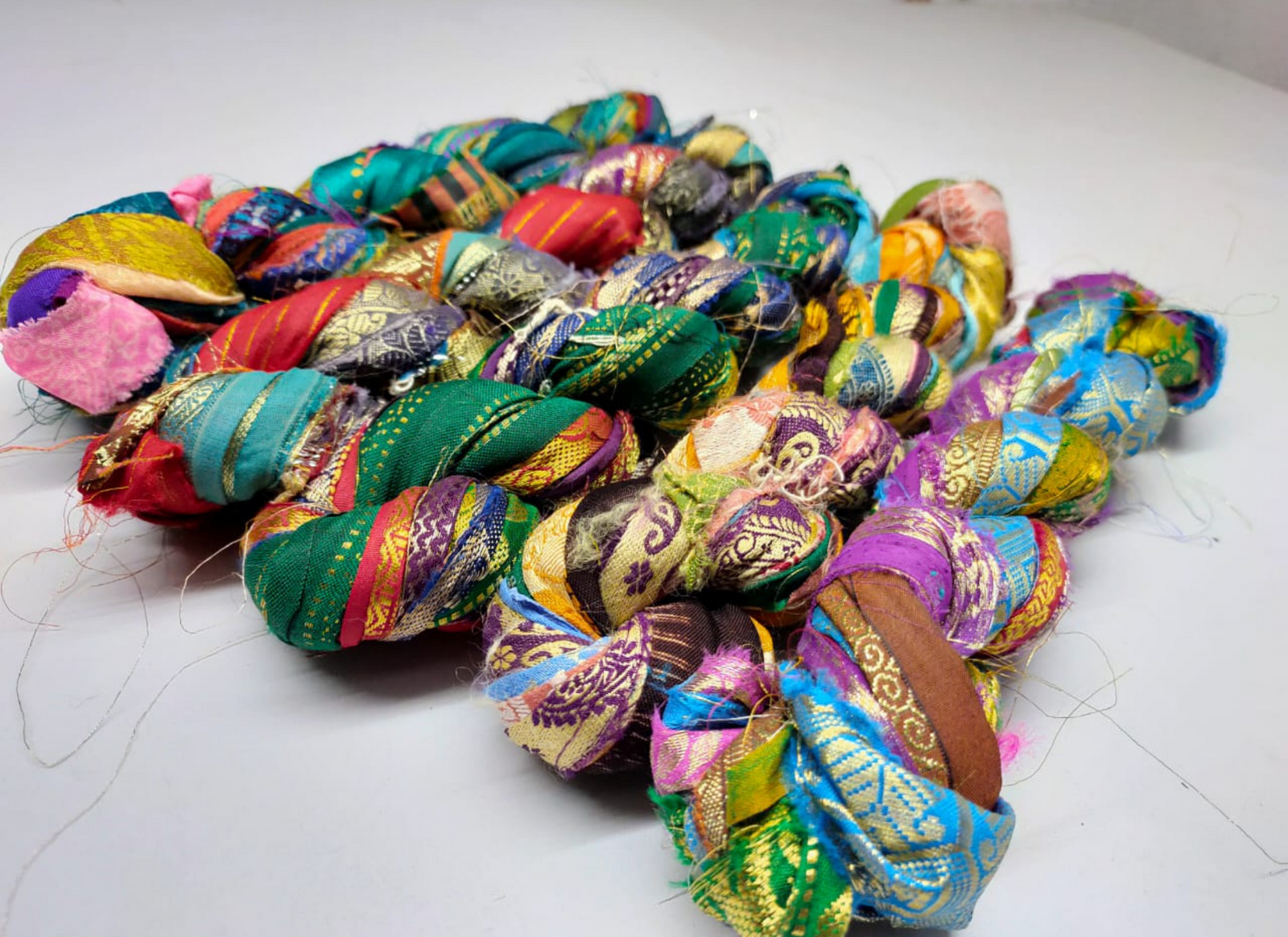 Recycled Lurex Sari Borders is the by-product of colorful saris that women wear in India. It is the loose ends of saris collected from industrial mills in India that is torn in stripes and sewn end to end to make beautiful and colorful ribbons. The vibrant colors and unique texture of these silk fabric, the sari silk ribbons are inspirational to designers, knitters, and artisans.